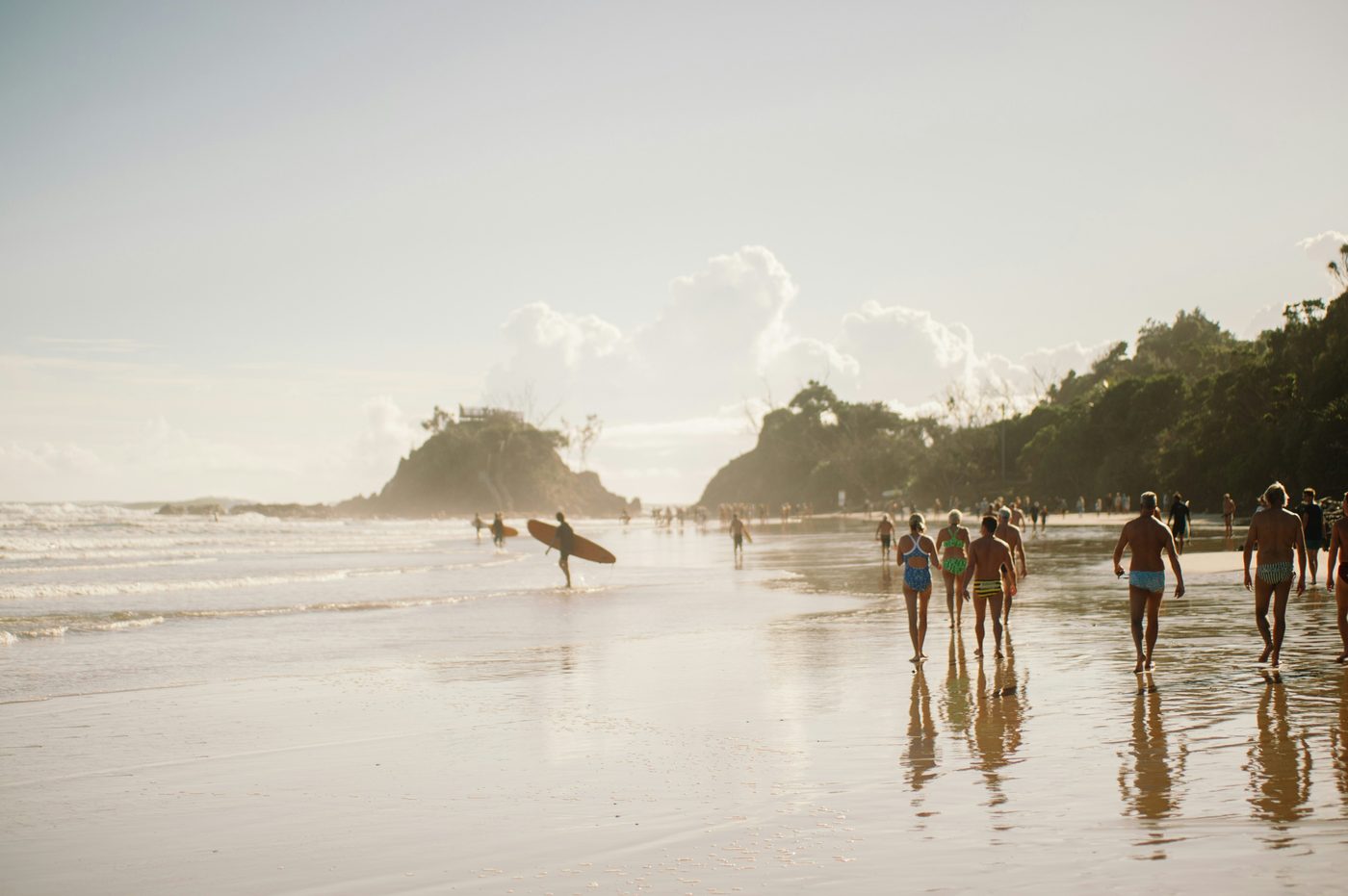 People walking along the wet sand at Byron Bay's main beach in golden afternoon light
