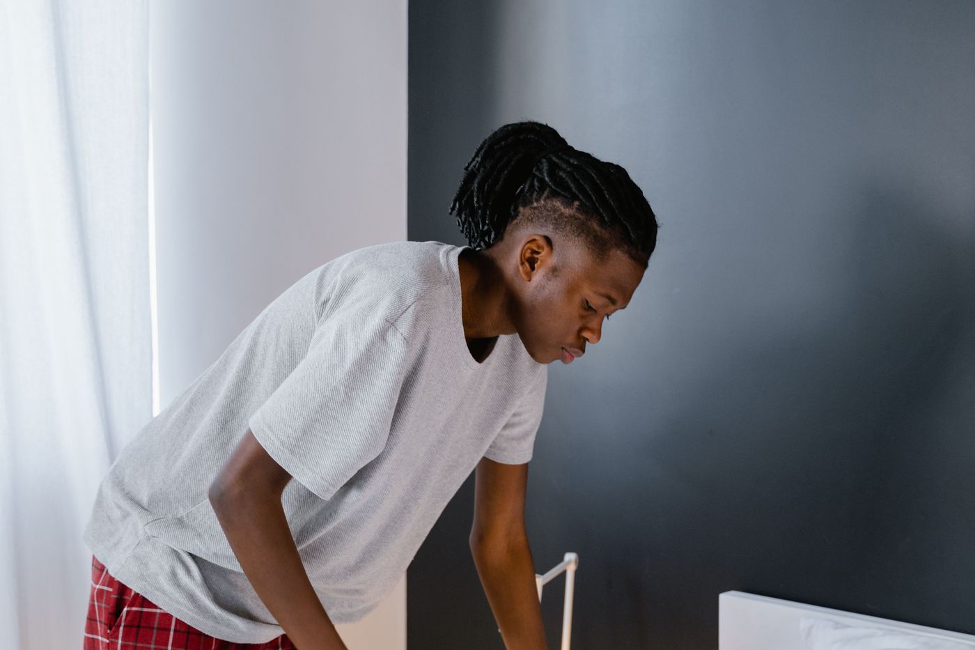 A young man tidying his bed at home in soft morning light
