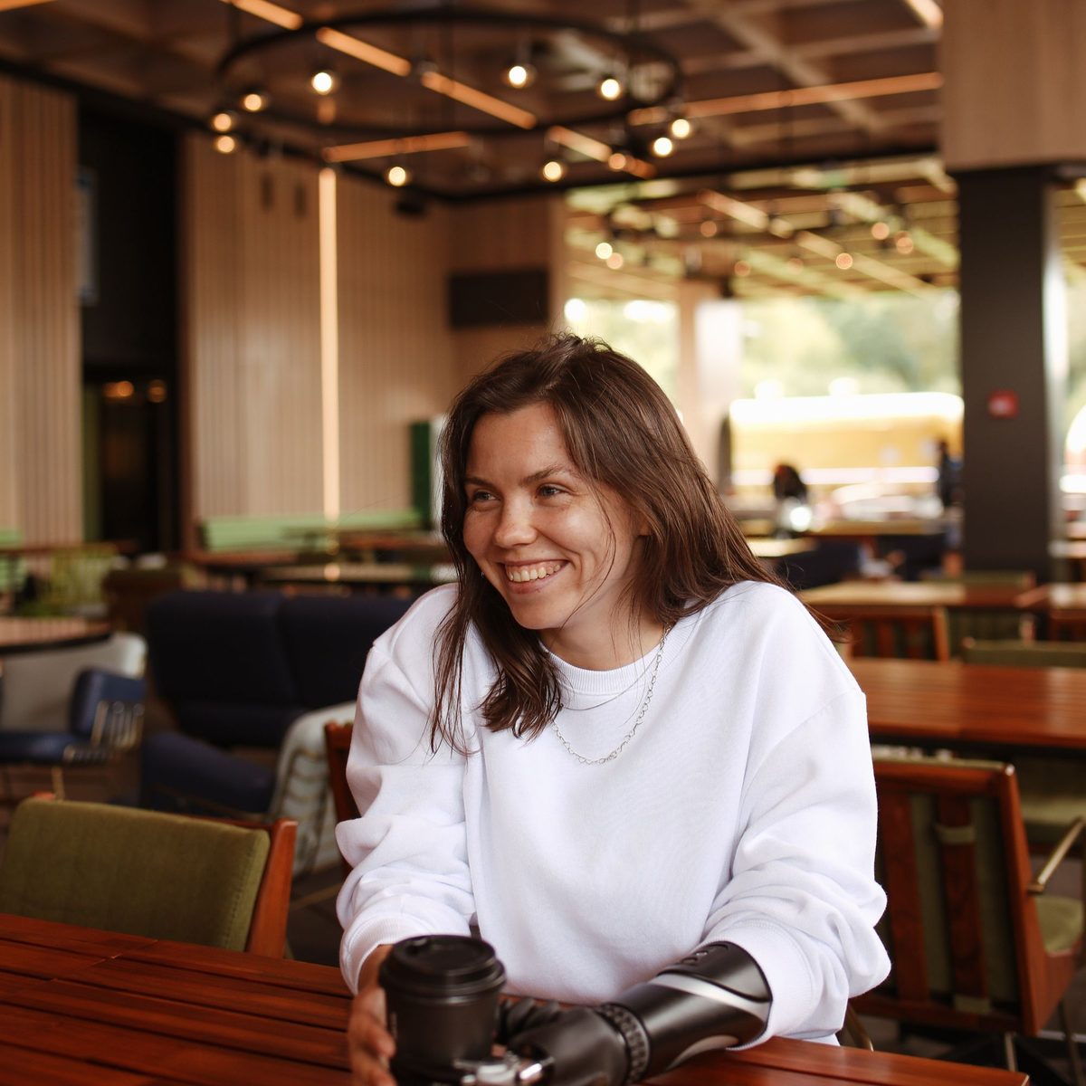 A woman smiling in a warm café, holding her coffee cup with her prosthetic hand