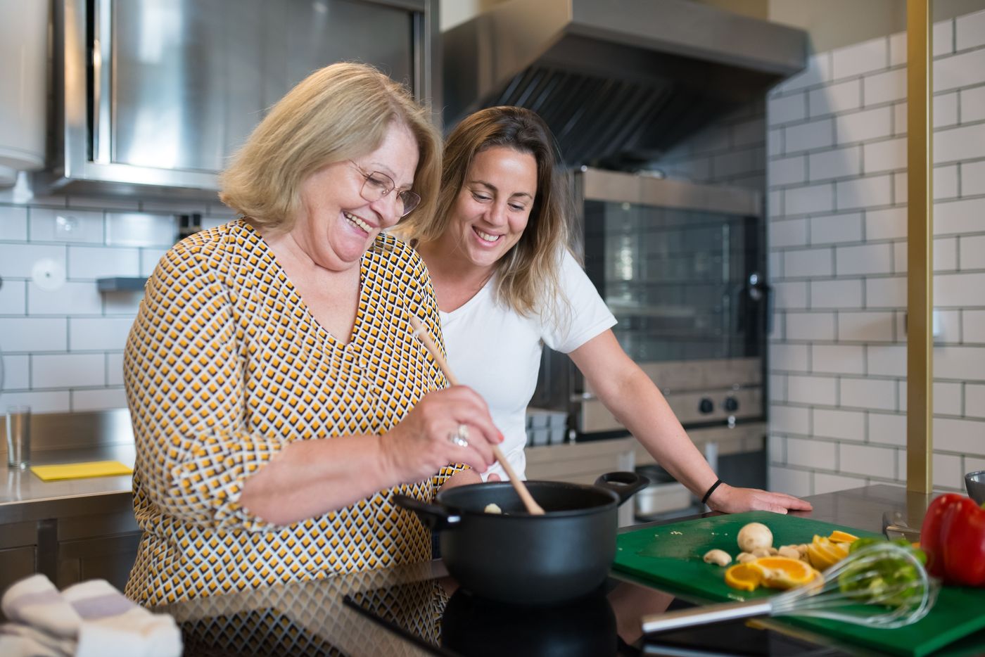 Two women laughing together while cooking dinner at home